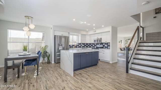 kitchen featuring hanging light fixtures, backsplash, stainless steel appliances, white cabinets, and light wood-type flooring