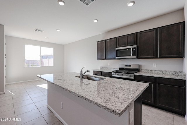 kitchen with sink, an island with sink, appliances with stainless steel finishes, light tile patterned flooring, and light stone counters