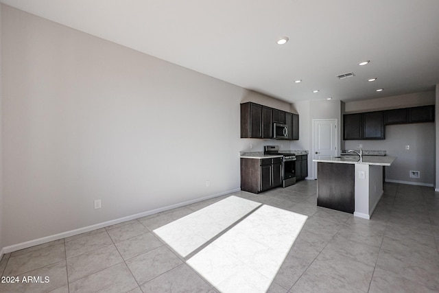 kitchen featuring a center island with sink, light tile patterned floors, stainless steel appliances, and dark brown cabinets