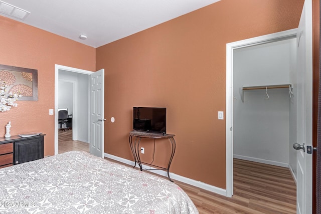 bedroom with a spacious closet, hardwood / wood-style flooring, and a closet