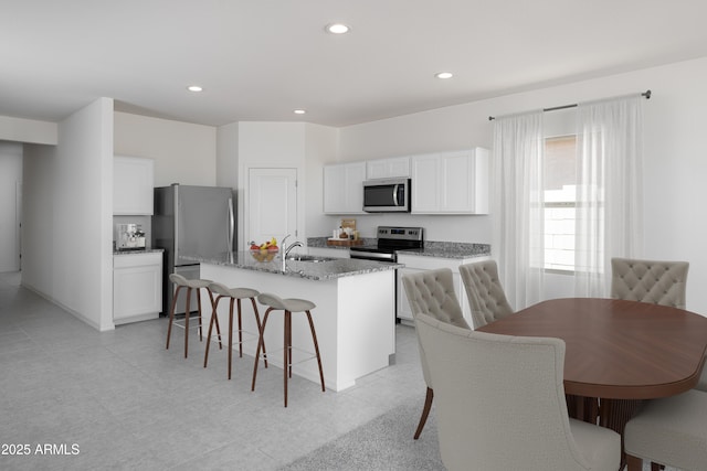 kitchen with appliances with stainless steel finishes, a kitchen breakfast bar, a center island with sink, a sink, and white cabinets