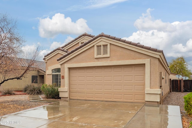 mediterranean / spanish-style house with concrete driveway, a tile roof, an attached garage, fence, and stucco siding