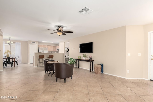 living room with ceiling fan with notable chandelier, visible vents, baseboards, and light tile patterned flooring