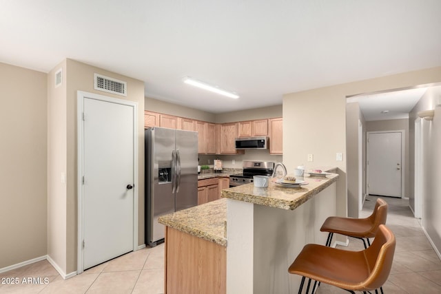 kitchen with visible vents, appliances with stainless steel finishes, a kitchen breakfast bar, a peninsula, and light brown cabinetry