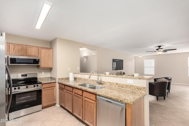 kitchen with light tile patterned floors, stainless steel appliances, a sink, light stone countertops, and a peninsula