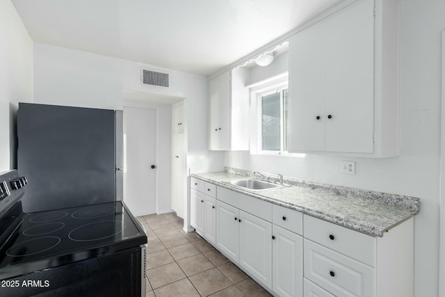 kitchen with sink, white cabinets, light tile patterned floors, electric stove, and stainless steel refrigerator