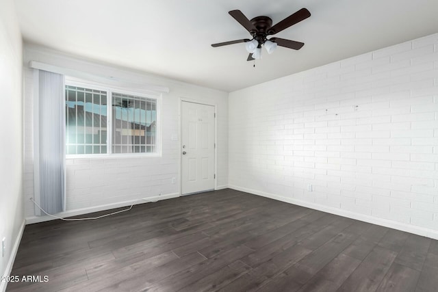 spare room featuring dark wood-type flooring, brick wall, and ceiling fan