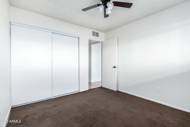 unfurnished bedroom with dark carpet, a textured ceiling, a closet, and ceiling fan