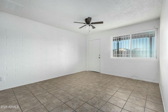 empty room with ceiling fan, brick wall, light tile patterned floors, and a textured ceiling