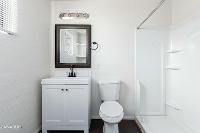 bathroom featuring brick wall, walk in shower, vanity, and toilet