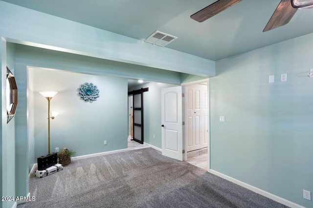 carpeted empty room featuring ceiling fan and a barn door