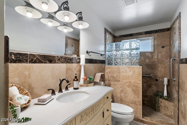 bathroom with a tile shower, vanity, tile walls, and toilet