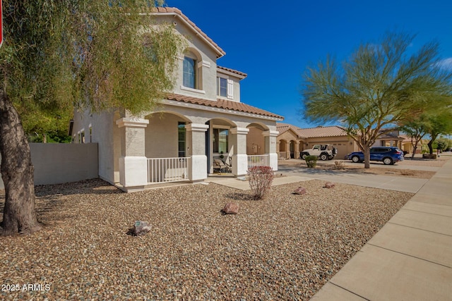 mediterranean / spanish house with covered porch, a tiled roof, concrete driveway, and stucco siding