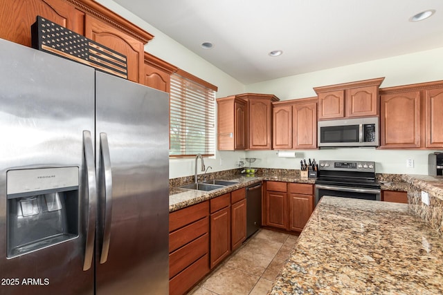 kitchen with brown cabinetry, appliances with stainless steel finishes, dark stone counters, and a sink