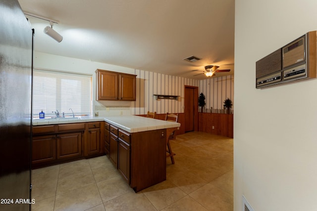 kitchen with kitchen peninsula, ceiling fan, tile countertops, stainless steel refrigerator, and sink