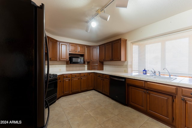 kitchen with light tile patterned floors, tile countertops, rail lighting, black appliances, and sink