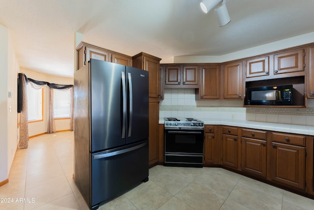 kitchen with tasteful backsplash, light tile patterned floors, stove, and stainless steel fridge