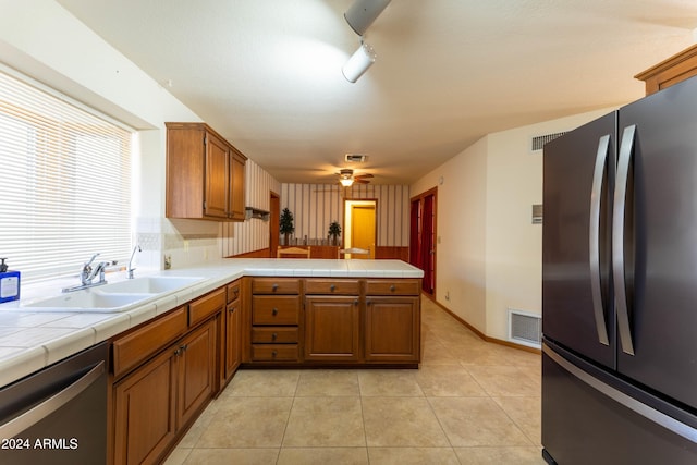 kitchen featuring kitchen peninsula, light tile patterned floors, tile countertops, sink, and stainless steel appliances