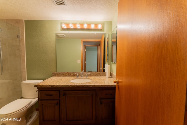 bathroom with vanity, toilet, a textured ceiling, and tiled shower