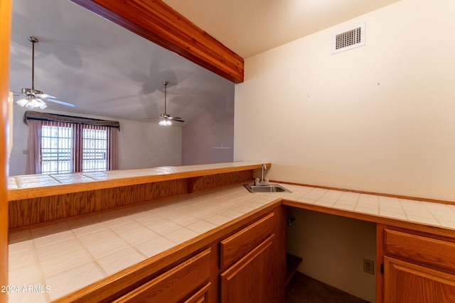 interior space with sink, lofted ceiling with beams, tile counters, and ceiling fan