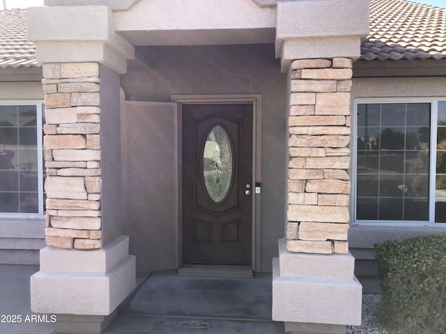 entrance to property featuring stucco siding, stone siding, and a tile roof