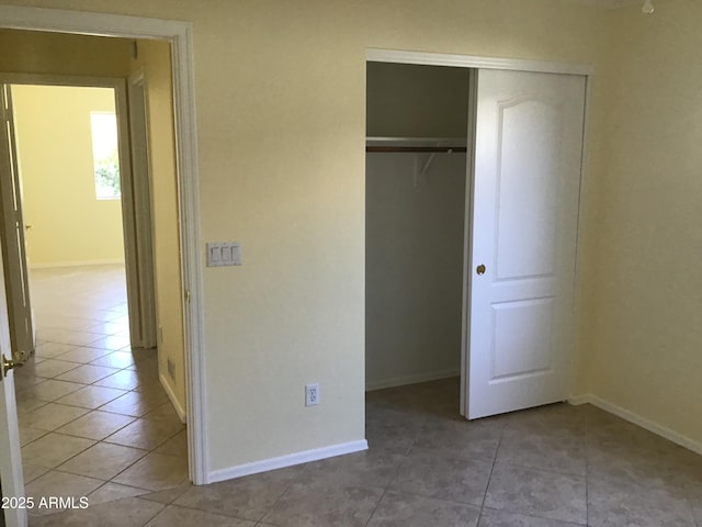 unfurnished bedroom featuring a closet, light tile patterned floors, and baseboards