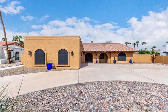 mediterranean / spanish house with a tile roof, driveway, fence, and stucco siding