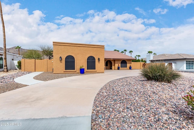 mediterranean / spanish-style house featuring a tile roof, fence, a gate, and stucco siding