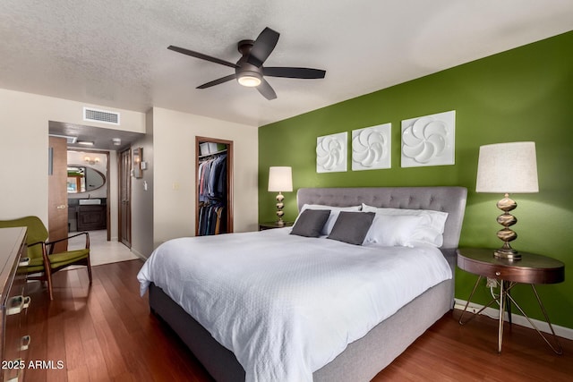 bedroom featuring a walk in closet, visible vents, a textured ceiling, and wood finished floors