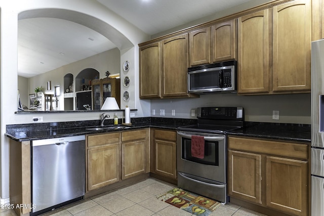 kitchen with dark stone countertops, sink, light tile patterned floors, and stainless steel appliances