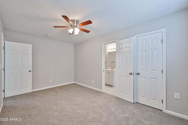 unfurnished bedroom featuring baseboards, ceiling fan, ensuite bath, and light colored carpet