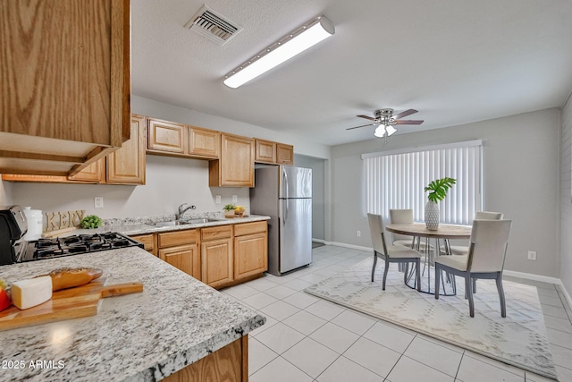 kitchen with a sink, light countertops, freestanding refrigerator, gas range, and visible vents