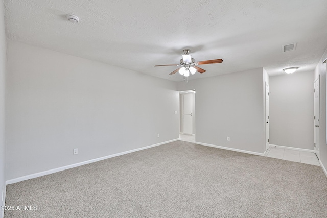 unfurnished room with light carpet, a textured ceiling, a ceiling fan, baseboards, and visible vents