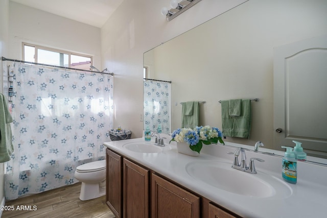 full bathroom with double vanity, toilet, wood finished floors, and a sink