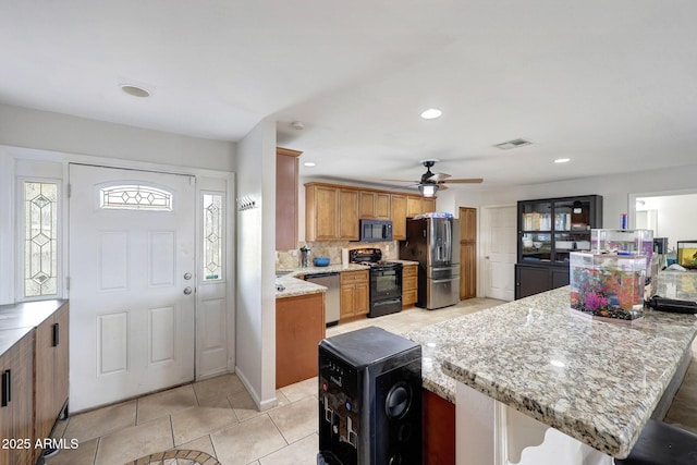 kitchen with light tile patterned floors, visible vents, brown cabinetry, light stone countertops, and black appliances