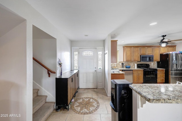 kitchen with appliances with stainless steel finishes, light tile patterned flooring, light stone countertops, and decorative backsplash