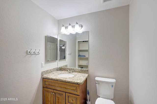 bathroom featuring toilet, a textured wall, and vanity