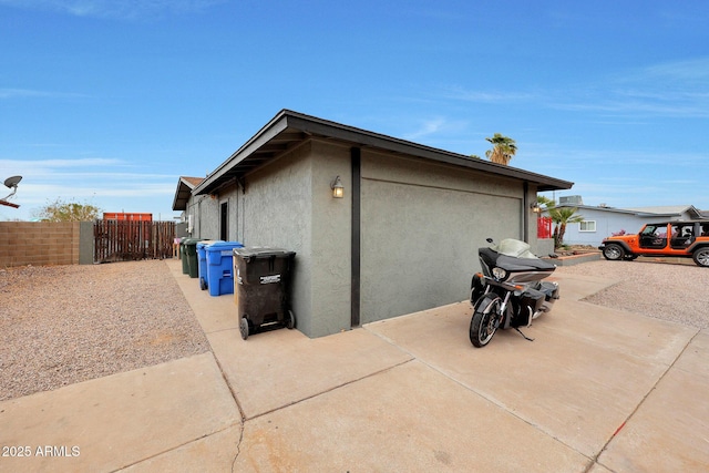 view of side of home featuring a patio, stucco siding, fence, a garage, and driveway