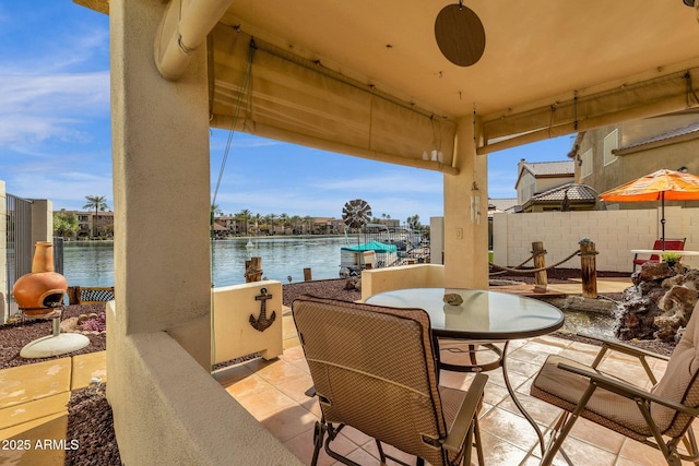 view of patio featuring a ceiling fan, outdoor dining space, a water view, and fence