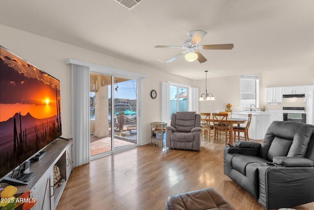 living area featuring ceiling fan with notable chandelier, light wood finished floors, and visible vents