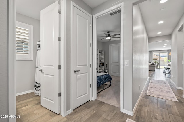hallway featuring visible vents, light wood-style flooring, baseboards, and recessed lighting