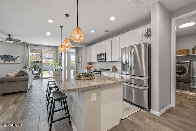 kitchen featuring wood finished floors, washer / dryer, stainless steel appliances, white cabinetry, and visible vents