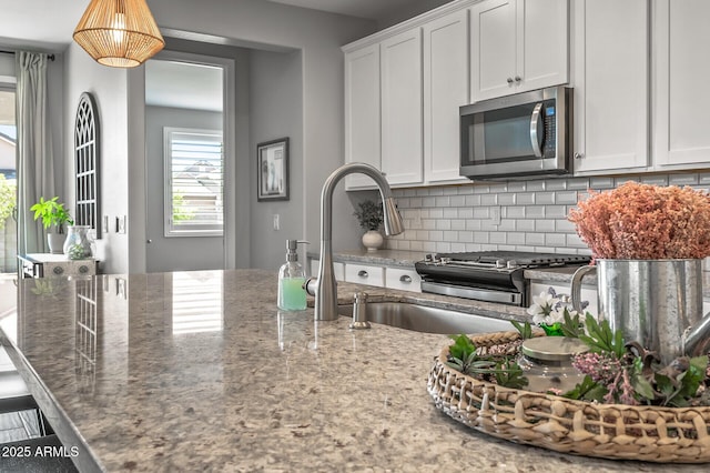 kitchen with stainless steel microwave, tasteful backsplash, white cabinets, and stone counters