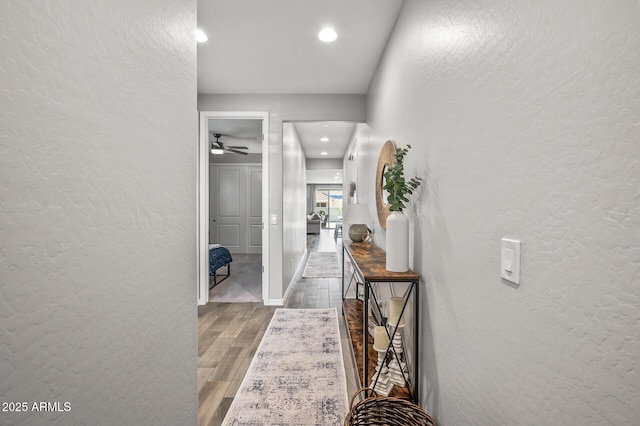 hallway featuring arched walkways, a textured wall, wood finished floors, and recessed lighting