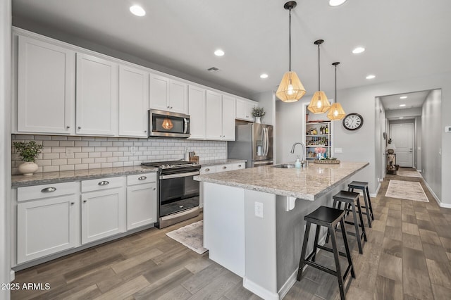kitchen with tasteful backsplash, wood finished floors, a sink, appliances with stainless steel finishes, and white cabinetry