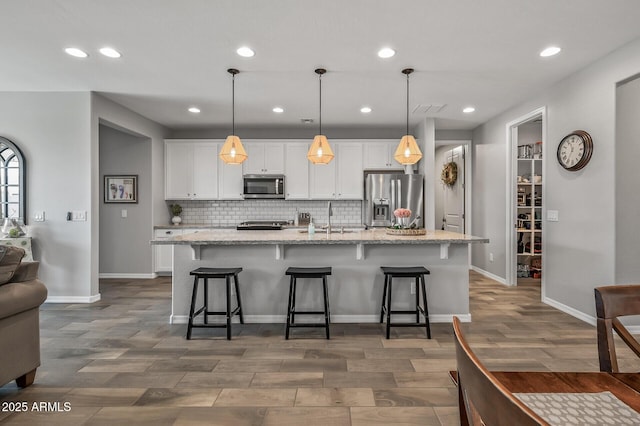 kitchen with white cabinets, stainless steel appliances, a large island with sink, and decorative backsplash