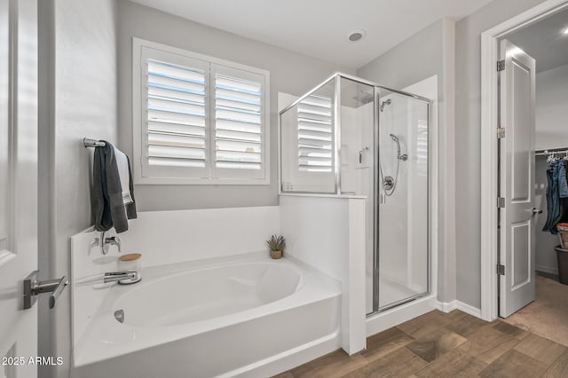 bathroom with a shower stall, a garden tub, a walk in closet, and wood finished floors