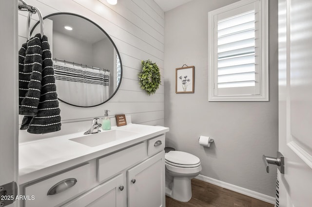 bathroom featuring wooden walls, wood finished floors, toilet, and vanity