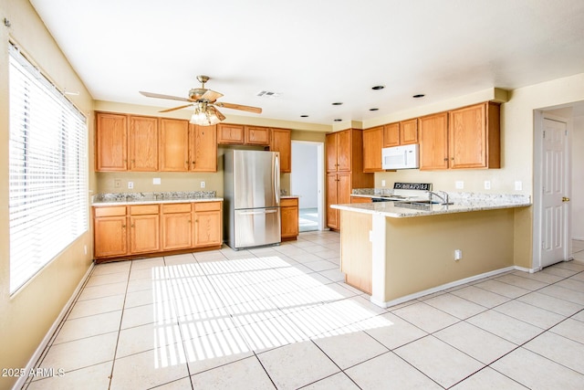 kitchen with stainless steel fridge, light tile patterned floors, ceiling fan, kitchen peninsula, and light stone countertops