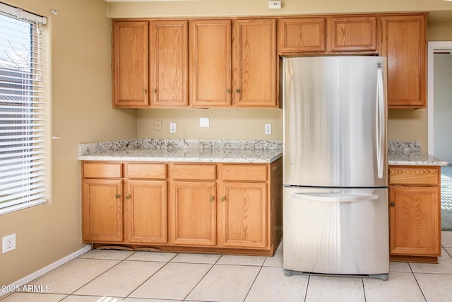 kitchen featuring light tile patterned floors, a wealth of natural light, light stone countertops, and stainless steel refrigerator